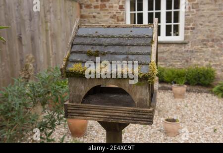 Traditional Weathered Wooden Bird House with a Slate Tile Roof Covered with Moss in a Country Cottage Garden in Rural Devon, England, UK Stock Photo