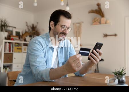Millennial man using card and phone to provide payment online Stock Photo