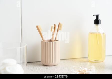 Cup with bamboo toothbrushes and bottle of soap placed on marble shelf against tiled wall in bathroom at home Stock Photo