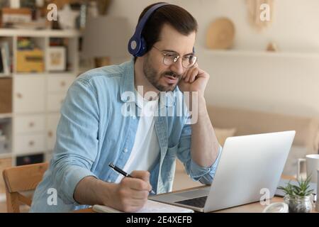 Young man getting remote education sitting by laptop in headphones Stock Photo