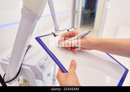 Doctor's hand is making notes on a clipboard or filling out a checklist Stock Photo