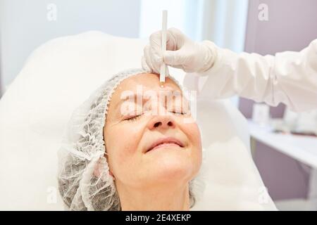 Elderly woman gets markings on her face for the facelift with hyaluronic acid dermal filler Stock Photo