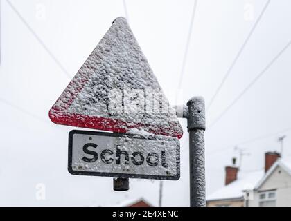 School sign covered in sleet crossing schools closed due to snow severe weather shut down warning freezing icy frozen heavy snowfall red triangle Stock Photo