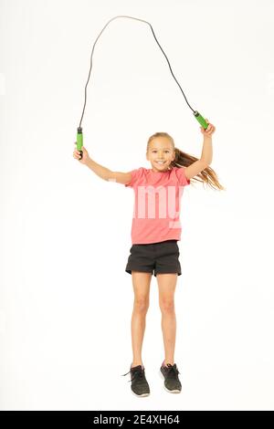 Adorable female child in sportswear looking at camera and smiling while holding jump rope. Isolated on white background Stock Photo