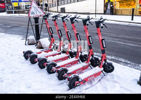 Birmingham, West Midlands, UK. 25th January 2021 - Voi electric scooters lined up in the snow on Dale End across the street from the Peaky Blinder pub. Credit: Ryan Underwood / Alamy Live News Stock Photo