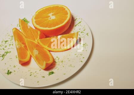 Top side view of a white plate with orange slices and half one and green leaf ornament Stock Photo