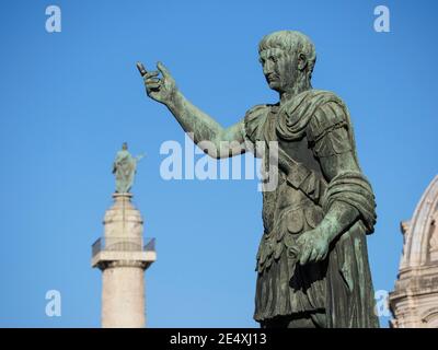 Rome. Italy. Bronze statue of Roman emperor Trajan on Via dei Fori Imperiali, Trajan's Column is in the background.   13th Emperor of the Roman Empire Stock Photo