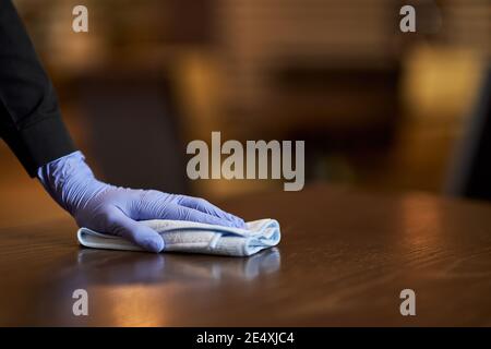 Cropped phot of hand in rubber glove holding cloth while wiping the wooden table clean Stock Photo