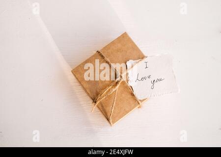 Valentine's day zero waste gift concept. Craft gift box with bow with small I love you note on white wooden background. Stock Photo