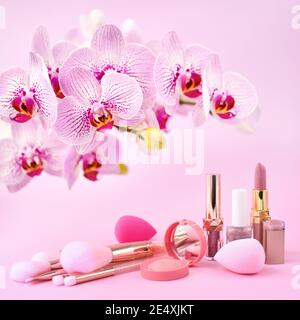 Orchid flowers and decorative cosmetics, sponges  and make-up brushes on a pink background Stock Photo