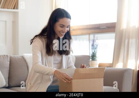 Overjoyed curious woman opening cardboard box with parcel at home Stock Photo