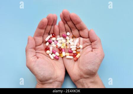 A man is holding a different pills in both his hands on blue background. Top view Stock Photo
