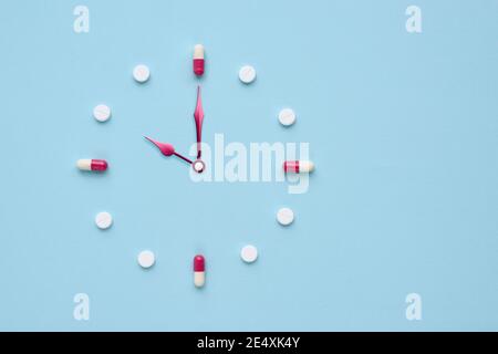 Clock created from pills and capsules on pastel blue background. Right time for using medicines. Flat lay. Stock Photo