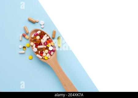 Wooden spoon full of pills, tablets and capsules on blue background, with empty space for text. Top view Stock Photo