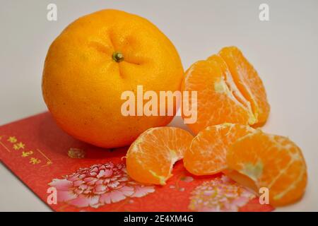 Close-up of Mandarin Oranges (Lukan) and peeled segments, with red envelope packets on white background Stock Photo