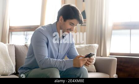 Close up smiling man using phone, sitting on cozy couch Stock Photo