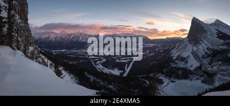 A panoramic sunrise view from the East End of Mount Rundle looking out over the town of Canmore and Ha Ling Peak across the valley gap. Stock Photo