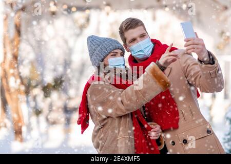 Couple in face masks taking winter selfie by smartphone Stock Photo