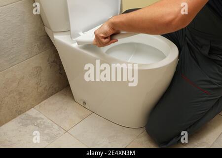 Plumber in overalls fixing a toilet seat by hand, bathroom toilet repair and plumbing service at home Stock Photo