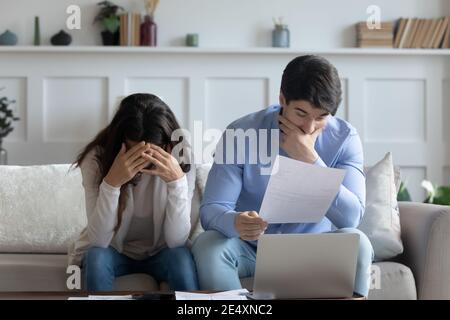 Frustrated young couple checking financial documents, reading bad news Stock Photo