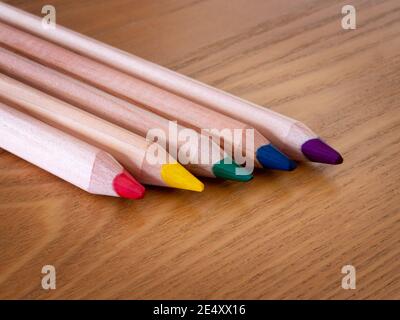 Five different colored pencils lines up on a wooden table Stock Photo