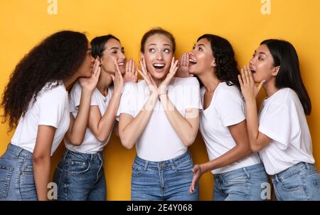 Excited Females Whispering Secrets Gossiping Sharing Rumors Over Yellow Background Stock Photo