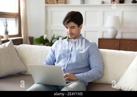 Focused man using laptop, sitting on couch at home Stock Photo