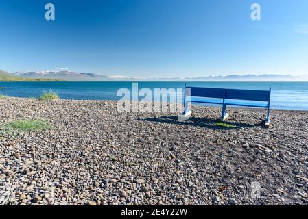 Empty wooden bench on a deserted pebble beach in Iceland on a clear summer day. Concept of loneliness, Stock Photo