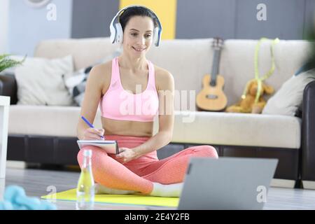 Woman in headphones and tracksuit making notes on notebook on online weight loss trainings concept Stock Photo