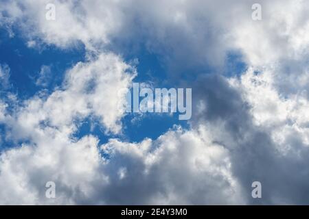 Bright blue sky shows through gaps in white-gray clouds. Meteorology, clouds and wind.  Changing weather from sunny to overcast. Weather forecast. Stock Photo