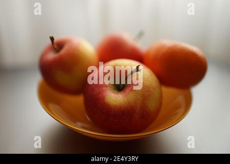 tangerine and three red apples in orange plate on the silver table. Stock Photo
