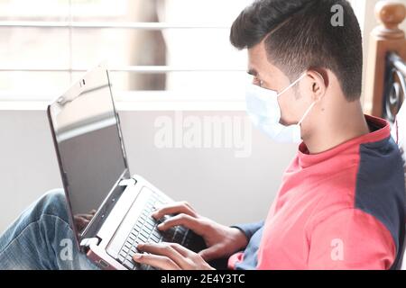 rear view of young man in surgical mask using laptop  Stock Photo