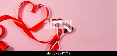 Valentine's day card, banner. Two red candy Lollipop hearts and red ribbon on pastel pink background. Banner of sweet heart shaped candies on pink bac Stock Photo