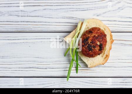 Fried meat cutlet with green onions on a piece of white bread. View from above Stock Photo