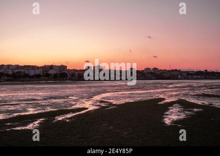 wideview of a city next  to a river bay in low tide during a pink golden sunset reflected in the water Stock Photo