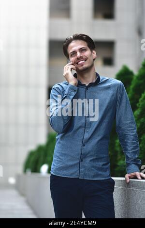 Nice positive guy in smart casual style is talking on the phone among the urban landscape. Stock Photo