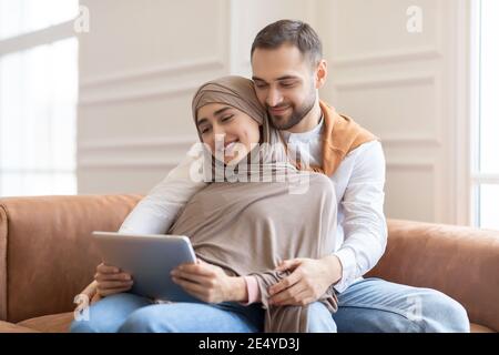 Muslim Couple Watching Movie On Tablet Sitting Sofa At Home Stock Photo