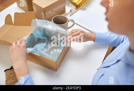 woman packing mug to parcel box at post office Stock Photo