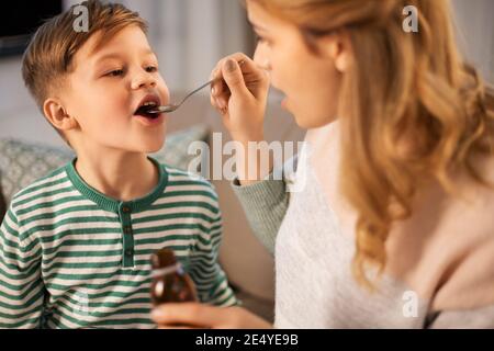 mother giving medication or cough syrup to ill son Stock Photo