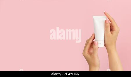 Woman hands holding unbranded plastic cosmetic tube on pink background. Banner with copy space Stock Photo