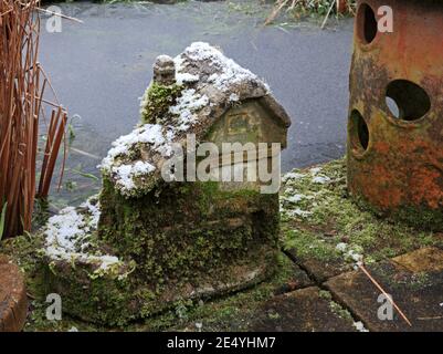 A moulded garden ornament of a watermill by a frozen pond in winter in Hellesdon, Norfolk, England, United Kingdom. Stock Photo