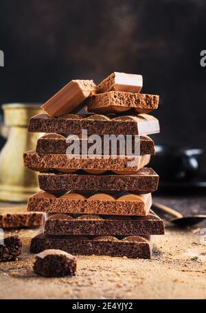 Stack of porous airy bitter and milk chocolate and cocoa on a dark background. Assorted different types of chocolate. Selective focus Stock Photo