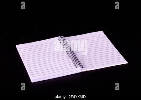 Opened A5 notepad with white lined pages and spiral boound with a black background Stock Photo