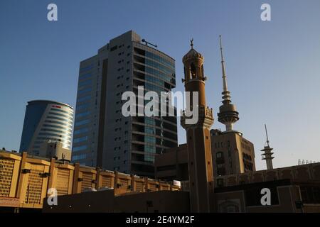 Kuwait City/Kuwait – January 10, 2021: Old mosque minaret with crescent symbol dwarfed by modern skyscrapers Stock Photo