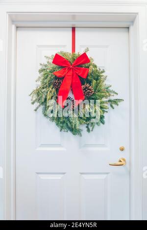 White appartment door with seasonal greens and red bow. Holiday decorations concept Stock Photo