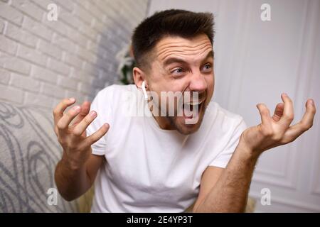 angry young man in earphones is talking to somebody on video call. man yelling Stock Photo