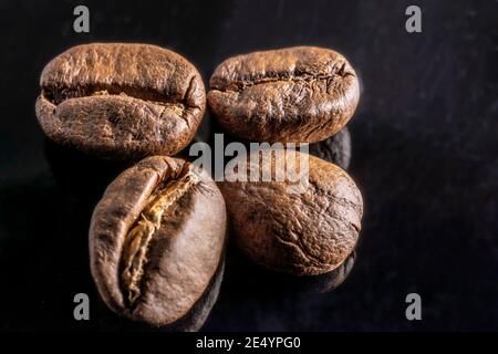 Coffee beans lie on the table, on black glass and are reflected in it Stock Photo
