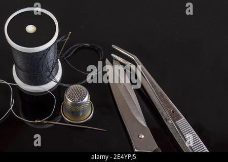 Spool of dark, black thread with needle and one metal thimble on