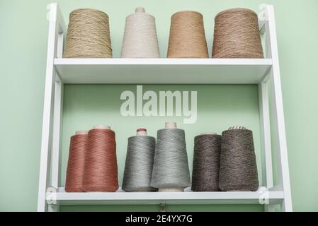 Set of colored threads for knitting on cone. Pile of big colorful spools of yarn on shelving Stock Photo