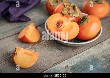 Fresh organic ripe Persimmon fruits in bowl with slice on old wooden background.